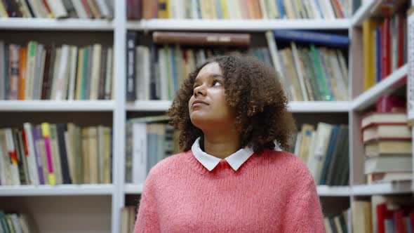 Black Girl Walking in Library Among Bookcases