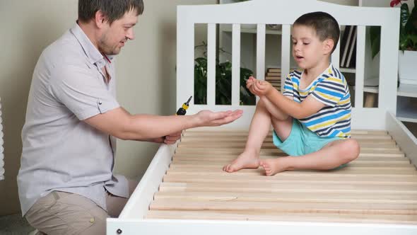 Father and Son Together Assemble a Children's Bed Screw Screws with a Screwdriver