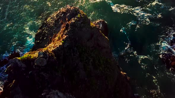 Overhead sunset view of rocky cliffs and green ocean waves in Big Sur California