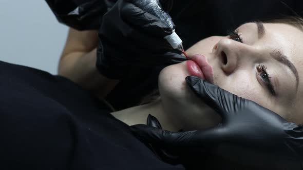 Cosmetologist Applying Pink Pigment Permanent Tattoo on Female Lips with Tatooing Needle Machine