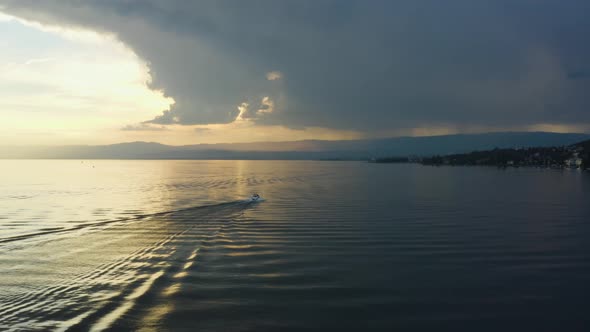 Following motorboat with drone at sunset. Yellow sunset with dark stormclouds. Lake Léman, Switzerl