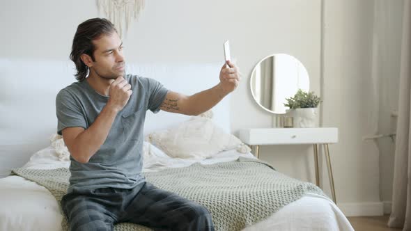 Good-looking Young Man Taking Selfie Using Smartphone Camera Sitting in Bed at Home