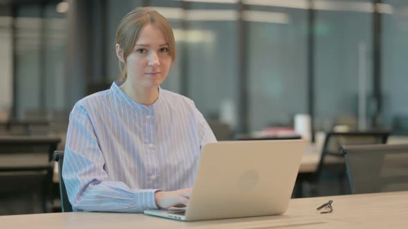 Young Woman Showing Thumbs Down Sign While Using Laptop in Office