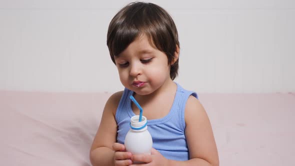 Baby Boy in Blue T-shirt Sitting on the Bed at Home and Drinking Milk