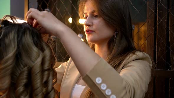 Hairdresser Doing Curly Hairstyle to Young Blonde Woman in Beauty Salon