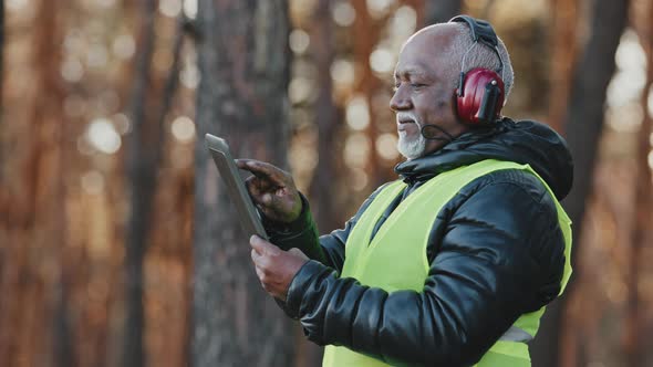 Elderly African American Forestry Engineer in Noiseisolating Headphones in Forest Old Mature Foreman