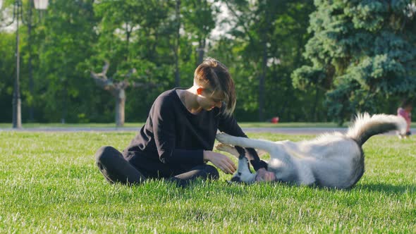 Beautiful Young Woman Playing with Funny Husky Dog Outdoors in Park