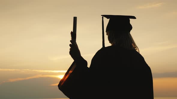 The Silhouette of a High School Graduate with a Diploma in His Hand Against the Sky