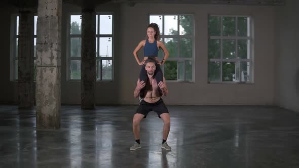 Athletic Shirtless Man Crouches with a Girl on His Shoulders in Empty Loft Studio