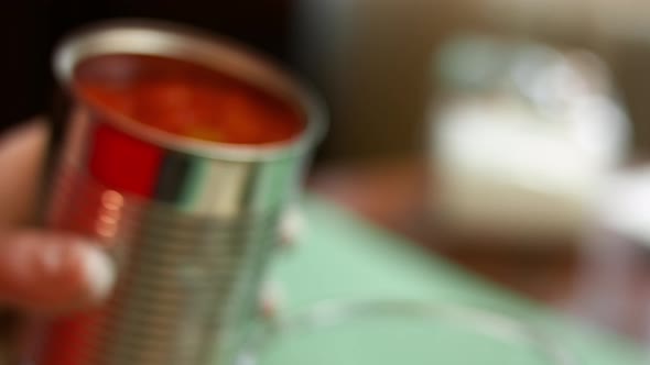 Pouring diced tomatoes from an open can into hand blender glass. Process of making salsa