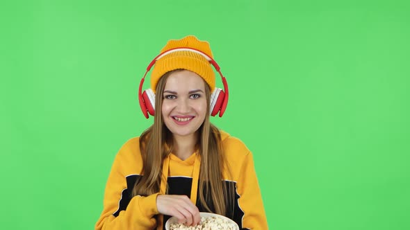 Portrait of Modern Girl in Big Red Headphones Is Enjoying Music and Eating Popcorn
