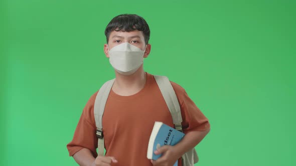 The Front View Of Asian Boy Student Wearing A Mask, Holding A Book And Running On Green Screen