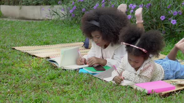 Happy African family with children lying reading or writing to book in the garden.