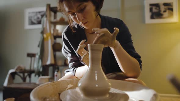 Young Female Potter Pulls the Neck of an Earthenware Vessel on Potter's Wheel