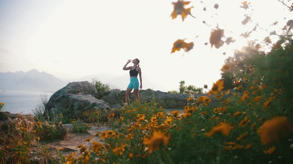 A Woman in Sportswear Drinks Water on the Hill