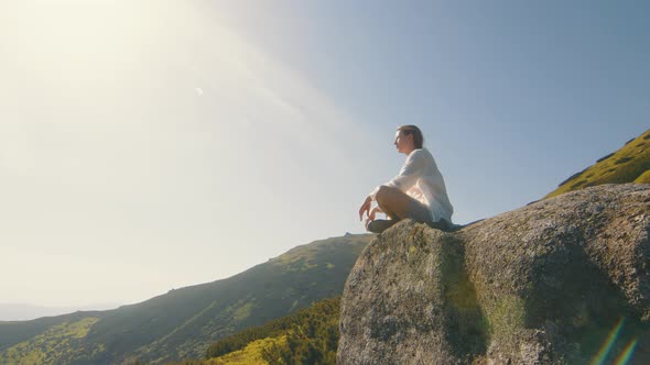 Girl Tourist Athlete Sitting on a Rock in the Mountains and Looking at the Beauty of Nature