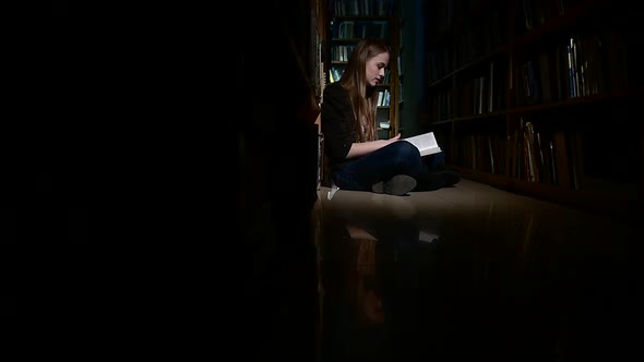 Student Girl Sitting on Floor and Examines Book in Library, Camera Moves Left To Right, Slow Motion