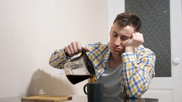Sleepy Man Pours Coffee While Sitting at the Table in the Kitchen