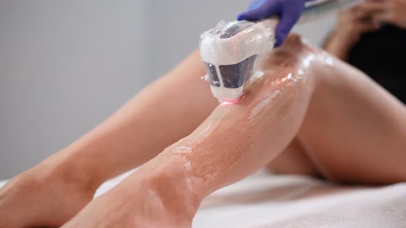 Beautician Doing Laser Hair Removal on Slim Legs Beautiful Woman in Beauty Salon