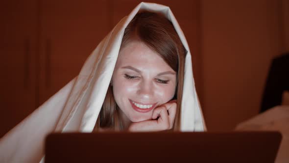 Relaxed Woman Lying on Bed Under Soft Blanket and Typing on Modern Laptop