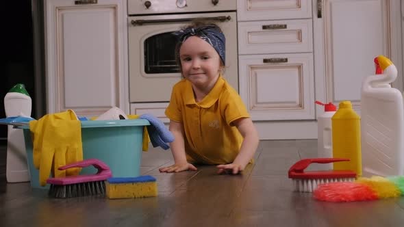 Portrait of Little Charming Girl at Home on the Floor Among Detergents and Rags.