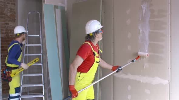 Worker Applying Primer To Wall with Long Roller on Construction Site