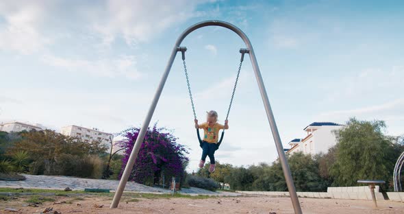 Slow motion cute european baby girl swinging on swing on chains in city park