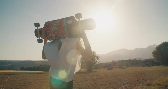 Stylish Young Adult Woman Walk at Sunset Holding Skate Longboard