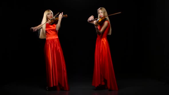 Two Women Playing the Fiddle. Studio. Black Background