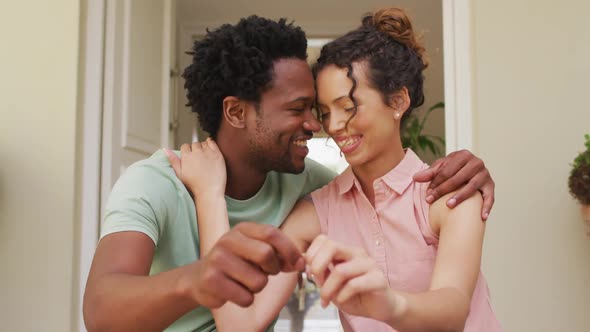 Happy biracial couple embracing with joy and holding keys in front of new house