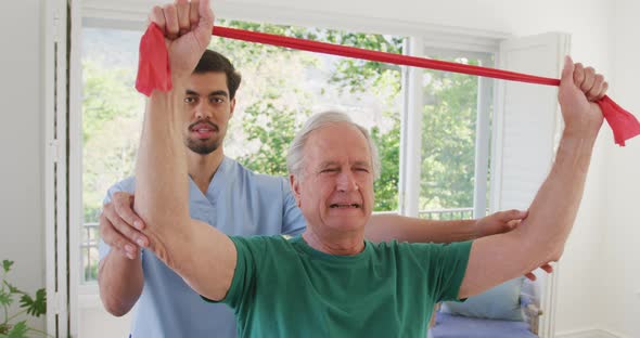 Biracial male physiotherapist with caucasian senior man holding resistance band while exercising