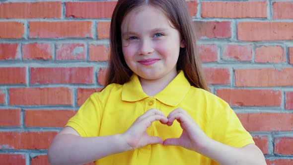 Little Girl Smiles Shows Heart Sign with Fingers