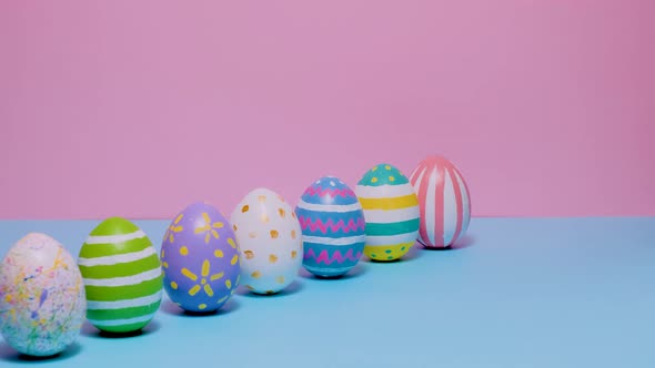 Colorful Painted Easter Eggs Roll and Knock Each Other on a Blue and Pink Background