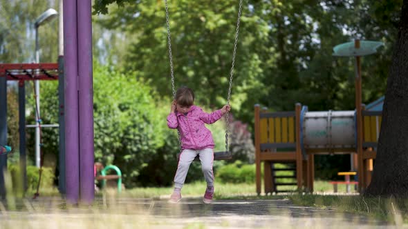 A Sad Lonely Girl is Slowly Swinging on a Swing in the Playground