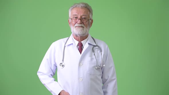 Handsome Senior Bearded Man Doctor Against Green Background