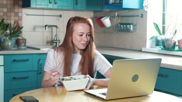 cheerful woman works at a laptop and eats a vegetable salad