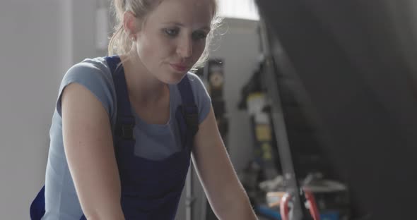 Professional female mechanic doing a car service, she is lifting a car hood and checking the engine