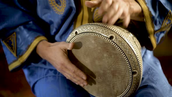 Tight shot of man in Moroccan dress playing arabic doumbek, darbuka, or derbeki