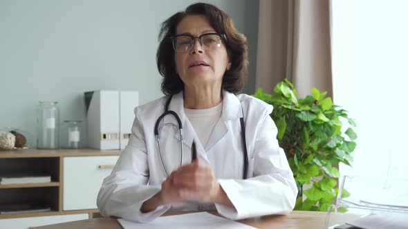 American Female Doctor Talking and Writing, Working at Table in Clinic Office Interior