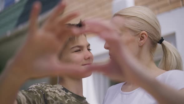 Closeup Heart Shape Hands with Woman and Boy Smiling Looking at Camera at Background