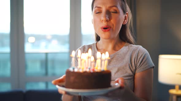 Happy Excited Woman Making Cherished Wish and Blowing Candles on Holiday Cake Celebrating Birthday