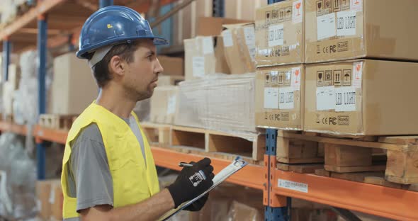 Logistics worker wearing a helmet working in a large warehouse checking inventory