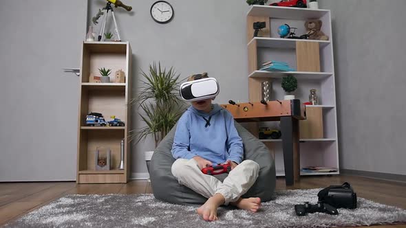 10-Aged Boy Sitting on Inflatable Sofa Sack Playing Games with Joystick Using Special VR