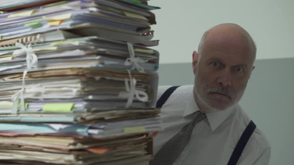 Stressed businessman peeking from behind a pile of paperwork