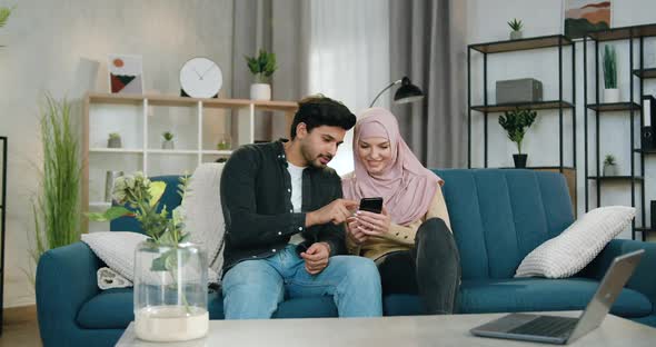 Muslim Couple in Love Sitting one Near One on Comfortable Sofa at Home and Watching videos