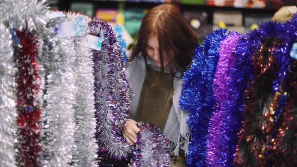 A Young Beautiful Woman Walks Around the Store and Selects Christmas Decorations and Decorations to