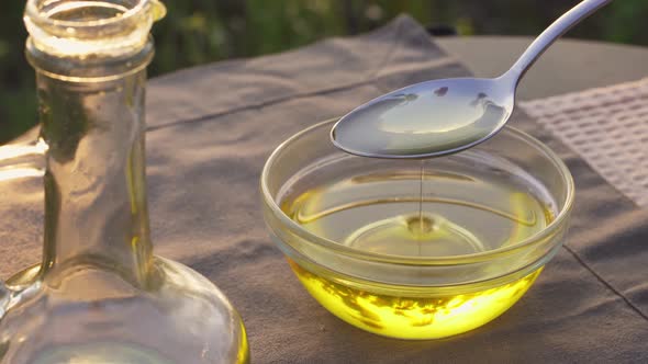 Vegetable Oil Flows Into Glass Bowl Outdoors. Glass Bottle Golden Oil In Sun. Organic Oil Production