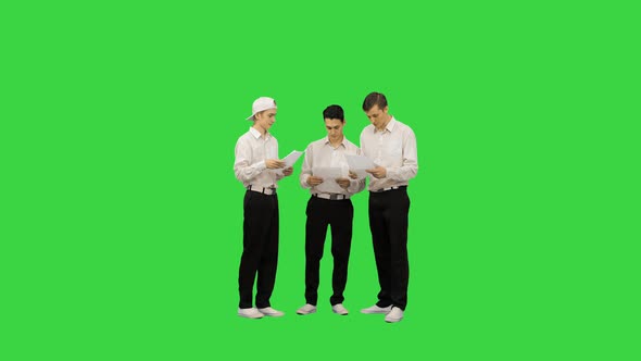 Three Similar Dressed Guys Reading Some Documents While One of Them Is Springing His Legs on a Green