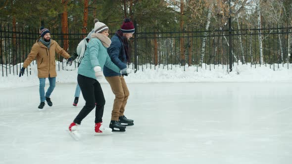 Slow Motion of Happy Men and Women Enjoying Ice-skating in Winter Park Holding Hands Laughing
