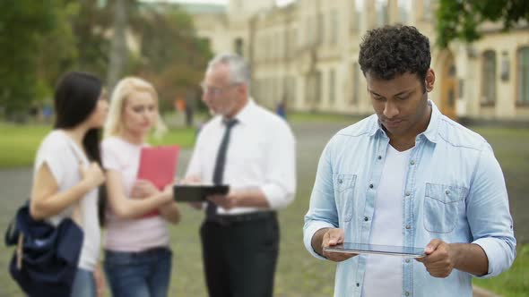 Hispanic man standing near college and doing homework on tablet, educational app